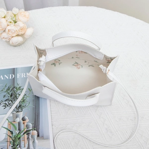 Elegant white crossbody handbag with floral lining and leather texture on knit background