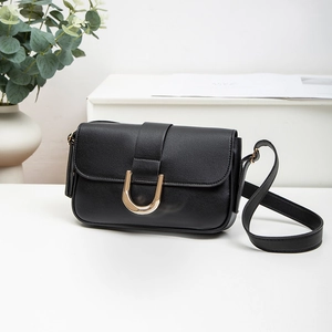 Fashionable black leather shoulder bag with gold U-shaped buckle in a minimalist setting