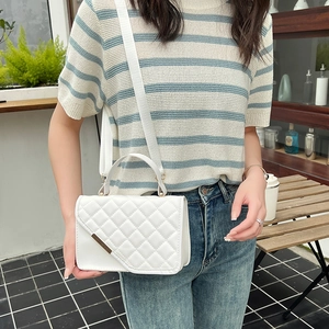 White quilted rhombic shoulder bag with adjustable strap worn by model in outdoor setting