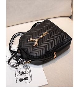 Close-up of black quilted backpack with golden deer charm and wide lettered strap