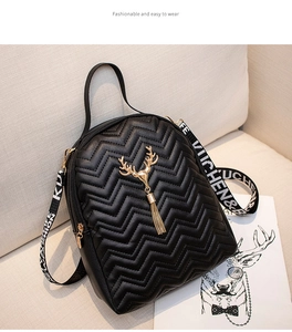 Detailed view of black quilted backpack with golden deer charm and jacquard strap on sofa