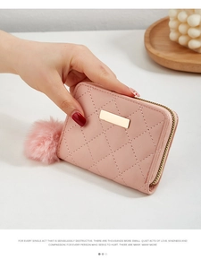 Détail du portefeuille rose matelassé avec plaque en métal et pompon moelleux