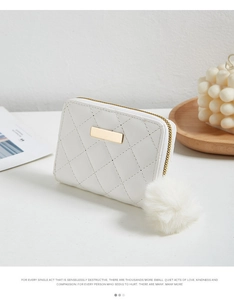 Détail du portefeuille matelassé blanc avec pompon et décor doré posé sur un plateau