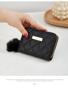 Détail d'un petit portefeuille matelassé noir avec plaque dorée et pompon décoratif doux
