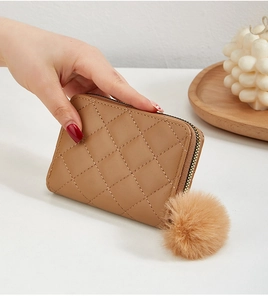 Détail d'un petit portefeuille matelassé marron avec pompon doux et fermeture éclair dorée