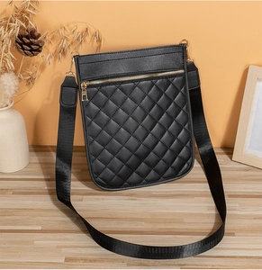 Close-up of black quilted crossbody bag with gold zippers on a wooden table setup