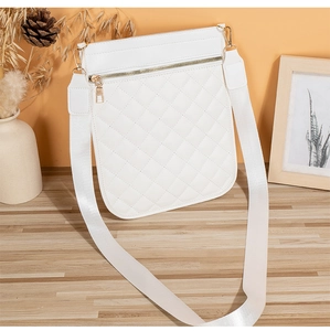 Close-up of quilted white crossbody bag with gold zippers on a textured wooden surface