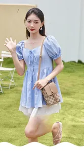 Détail du petit sac bandoulière beige à carreaux porté sur une robe à carreaux bleus