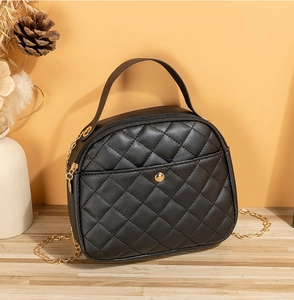 Close-up of black quilted shell bag with gold chain strap on a wooden surface