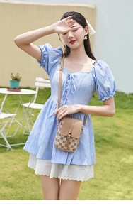 Petit sac à bandoulière marron à carreaux porté avec une robe d'été sur de l'herbe
