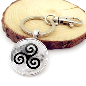 Detail of silver wolf moon triskelion keychain on a wooden rustic decorative base