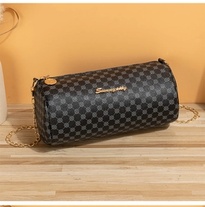 Detail of cylinder crossbody bag featuring golden chain strap and floral pattern on black PU