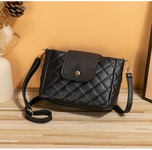 Detail of black quilted bucket bag with gold circular clasp and adjustable strap on a wooden table