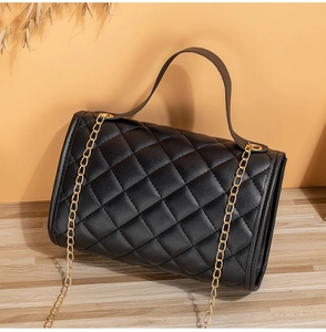 Detailed view of black quilted leather handbag with gold chain strap and stitching detail