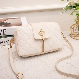Elegant cream quilted crossbody bag with golden crown buckle and tassel on table