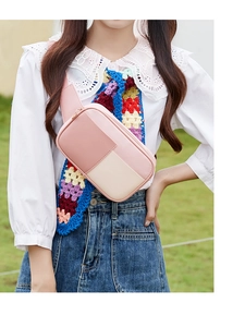 Gros plan d'un sac bandoulière rose et beige porté par un mannequin en plein air