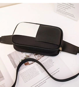 Detail view of a black and white leather waist bag with a gold zipper on a magazine