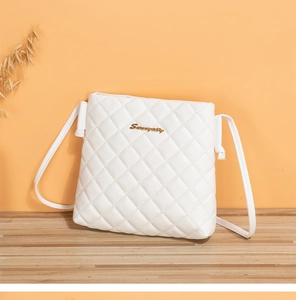 Détail du sac bandoulière matelassé blanc avec logo doré sur surface en bois