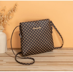 Détail d'un sac bandoulière marron avec logo doré sur une surface en bois clair