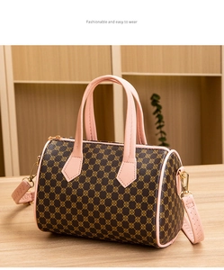 Detail of cylinder Boston bag with floral print and pink leather handles on a wooden table
