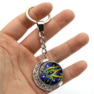Silver crescent moon keychain with rotating Eye of Horus glass pendant held by hand