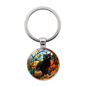 Detail of round keychain with stained glass art showing black cat, pumpkin and autumn leaves
