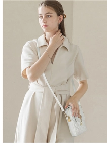 Detail of white quilted crossbody phone bag featuring a golden crown and pearl charm