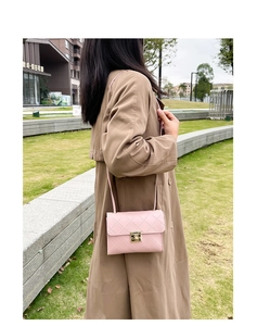 Detail of pink quilted crossbody bag with gold rectangular twist lock on a lawn background