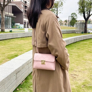 Elegant pink quilted crossbody bag with gold lock shown in a stylish outdoor park setting