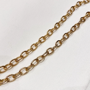 Detailed close-up of a polished gold oval link chain strap on white twill fabric texture