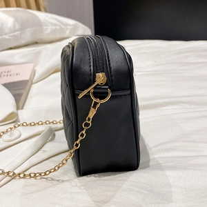 Detail view of black quilted crossbody bag showing gold zipper and metal chain hardware