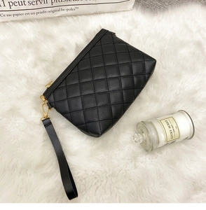 Close-up of black quilted leather handbag with gold metal zipper and leather wristlet