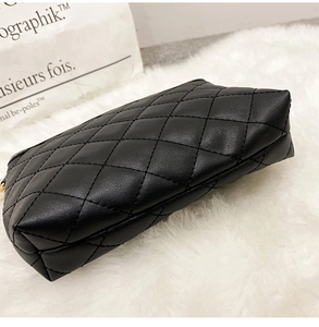 Detail of classic black quilted crossbody bag with golden zipper on white plush background