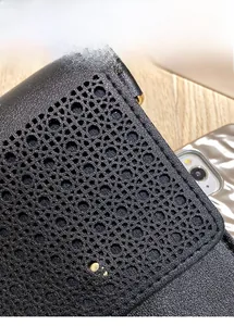 Detail of black leather phone bag featuring a laser-cut hollow pattern and gold buckle