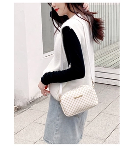 Close-up of white crossbody bag with geometric pattern and gold hardware on female model