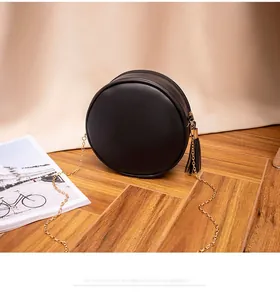 Detail of a black round crossbody bag with golden chain strap and tassel on wood surface