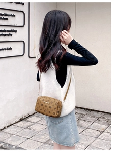 Detail shot of a tan crossbody bag with heart pattern and gold metal trim on a model