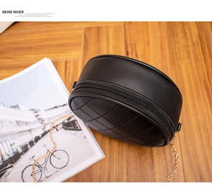 Detail of black quilted round bag featuring gold chain strap on a wooden surface