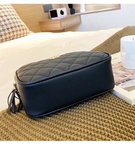 Detail of black quilted leather crossbody bag with gold logo and tassel on knit blanket