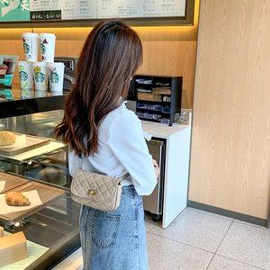 Beige quilted waist bag with golden twist lock worn by model in a bright cafe setting