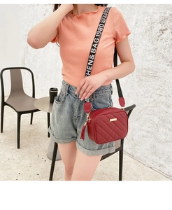 Red quilted crossbody bag with wide lettered strap and fringe detail worn by a model
