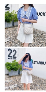 Detail of light gray crossbody bag featuring V-shaped quilting and wide lettered strap