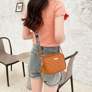 Brown quilted crossbody camera bag with wide lettered strap shown on a model in a casual setting