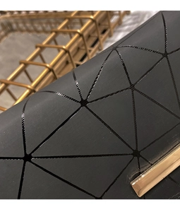 Detail of matte black geometric puzzle surface with elegant gold metal accent on long wallet