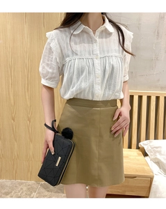 Close-up of a stylish quilted clutch bag paired with a lace shirt and green skirt