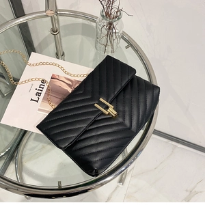 Close-up of black V-quilted faux leather bag with golden rectangular lock and chain strap
