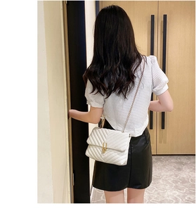 Rear view of a model wearing a white V-quilted crossbody bag with a gold chain strap