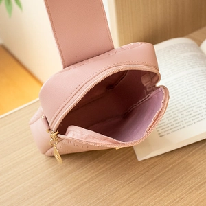 Pink leather crossbody phone bag with embossed pattern and golden zipper on a desk