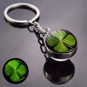 Close-up of luminous four-leaf clover glass ball keychain with glowing green night effect