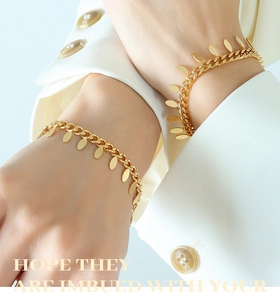 Close-up of gold chain bracelet with oval pendants on a model wearing white suit